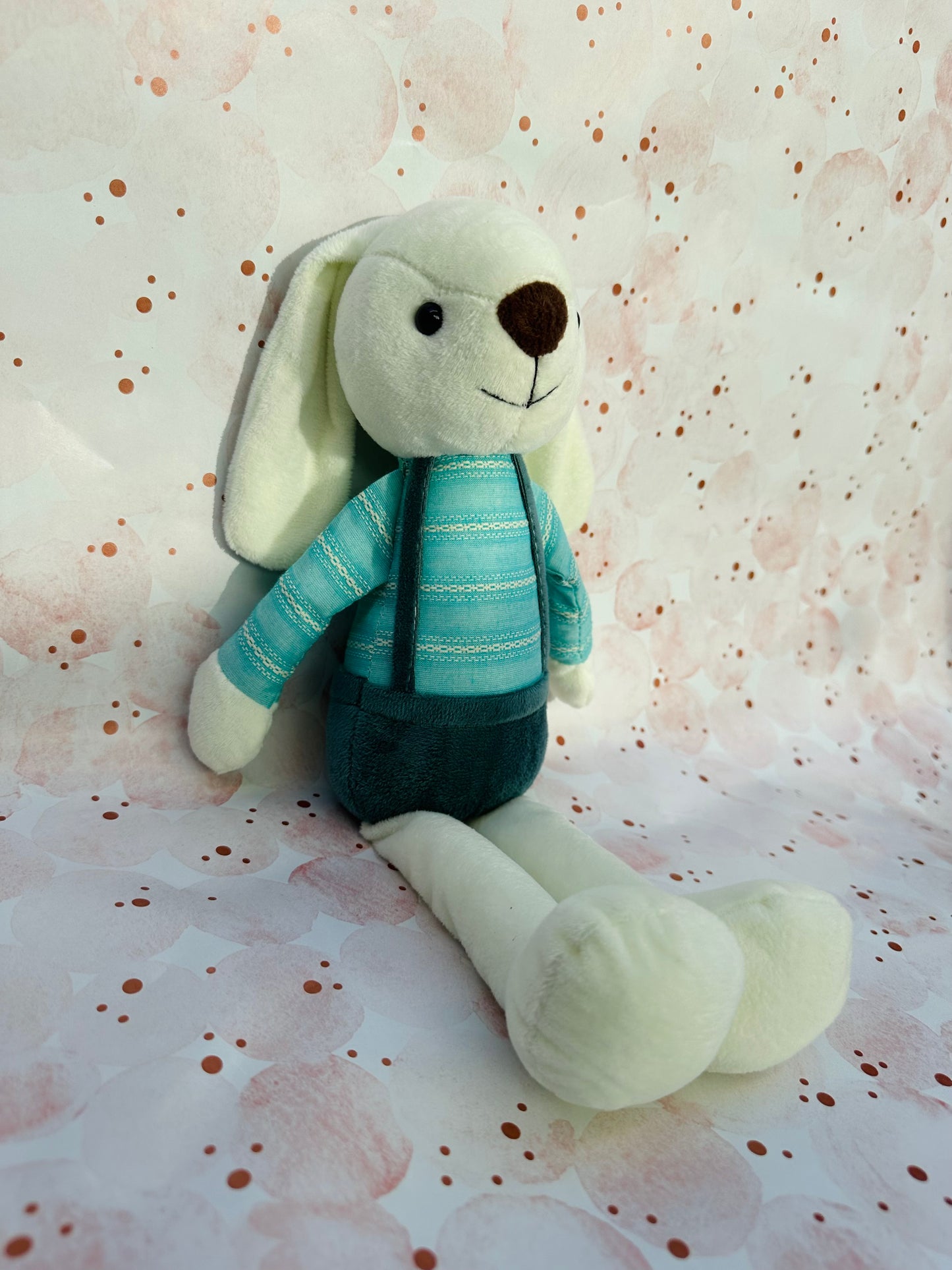 Plush toy rabbit with a blue sweater on a patterned background