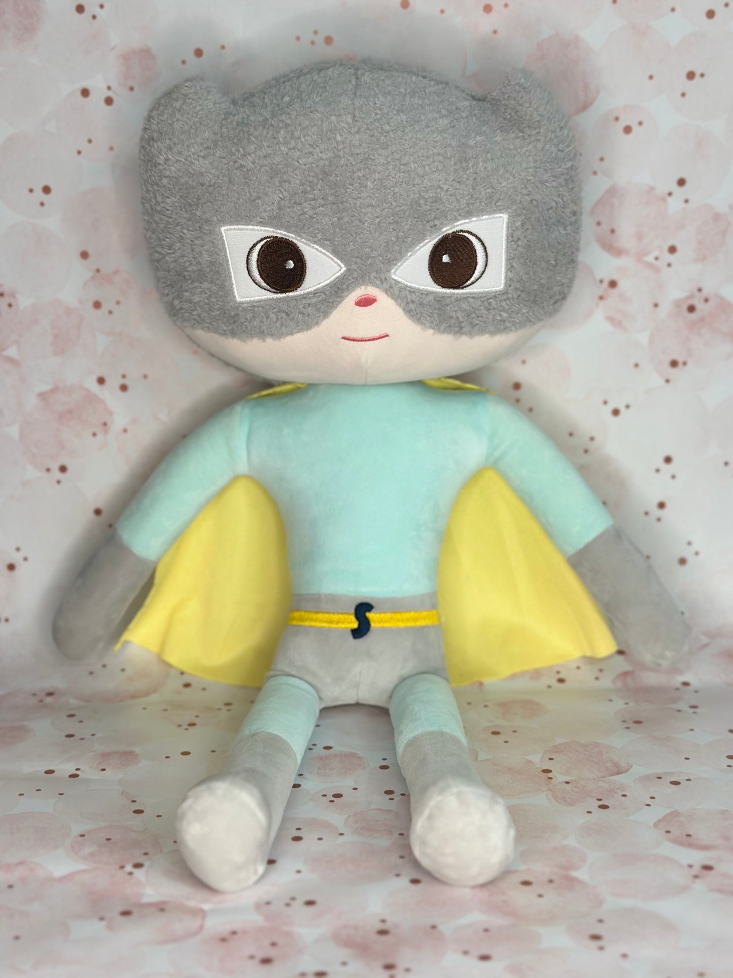Plush toy with a superhero mask and cape on a patterned background