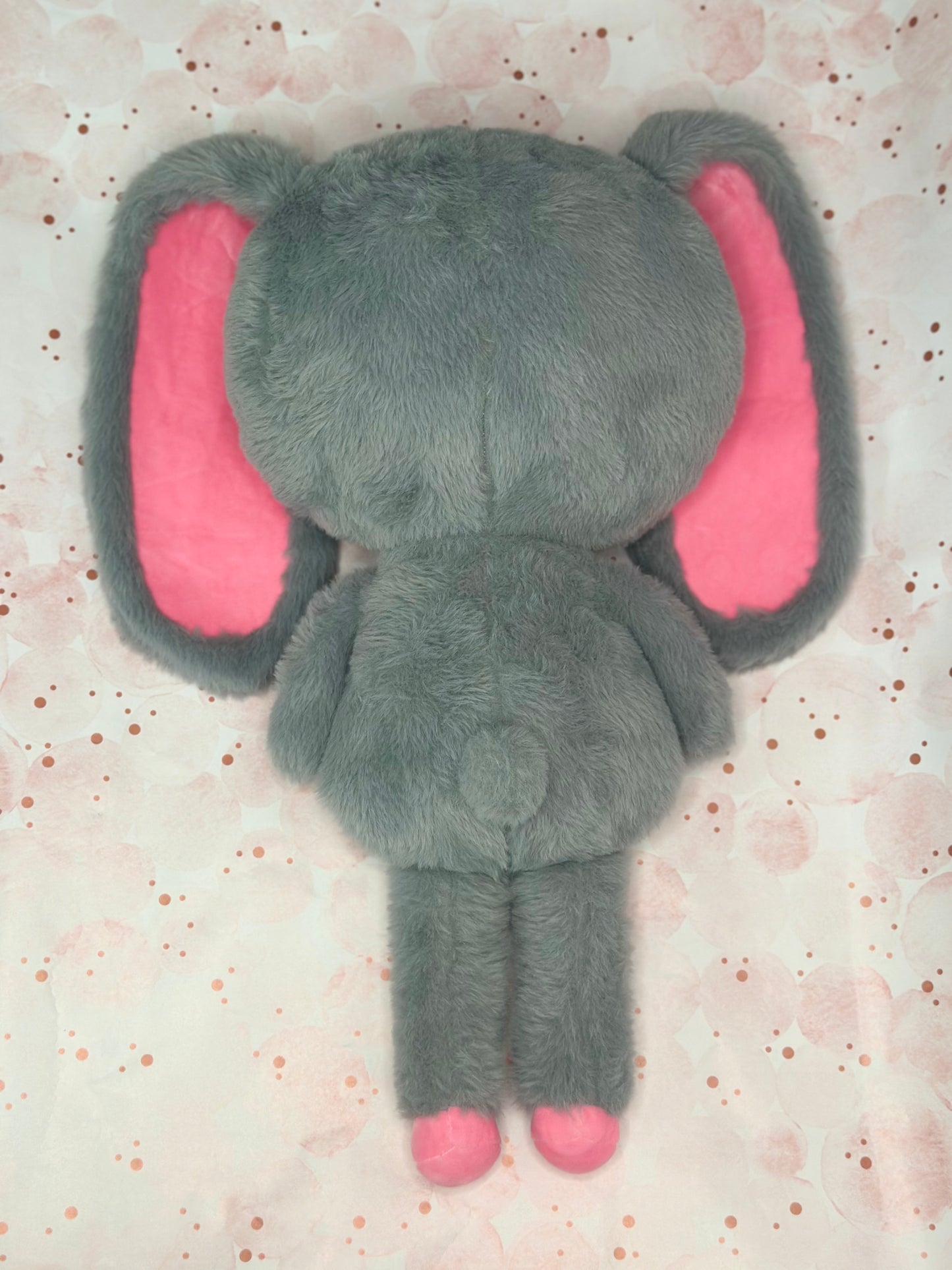 Gray plush bunny toy with pink ears on a light pink background
