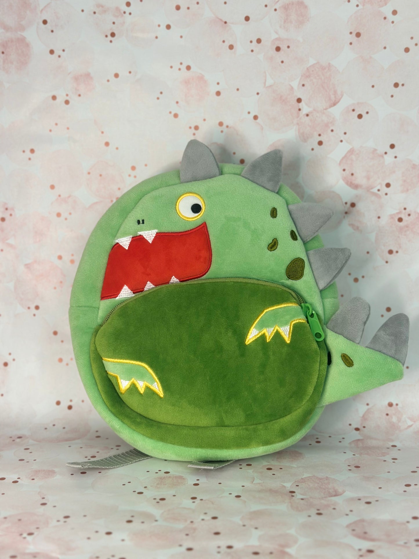 Green dinosaur-shaped backpack on a light pink background