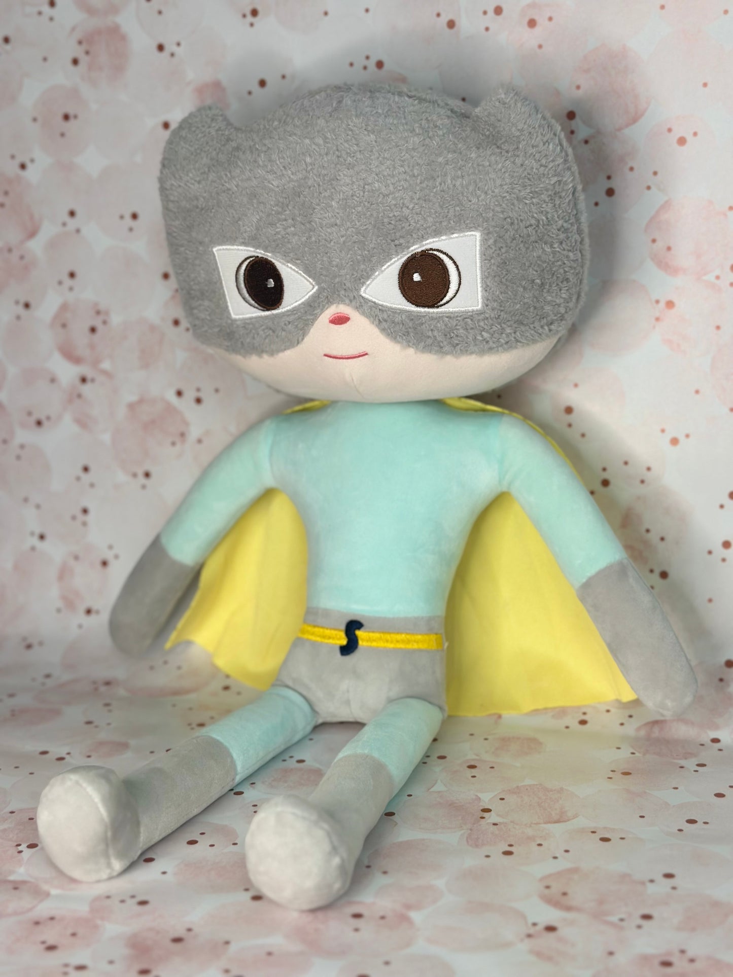 Plush toy with gray hair, light blue shirt, and gray pants on a patterned background