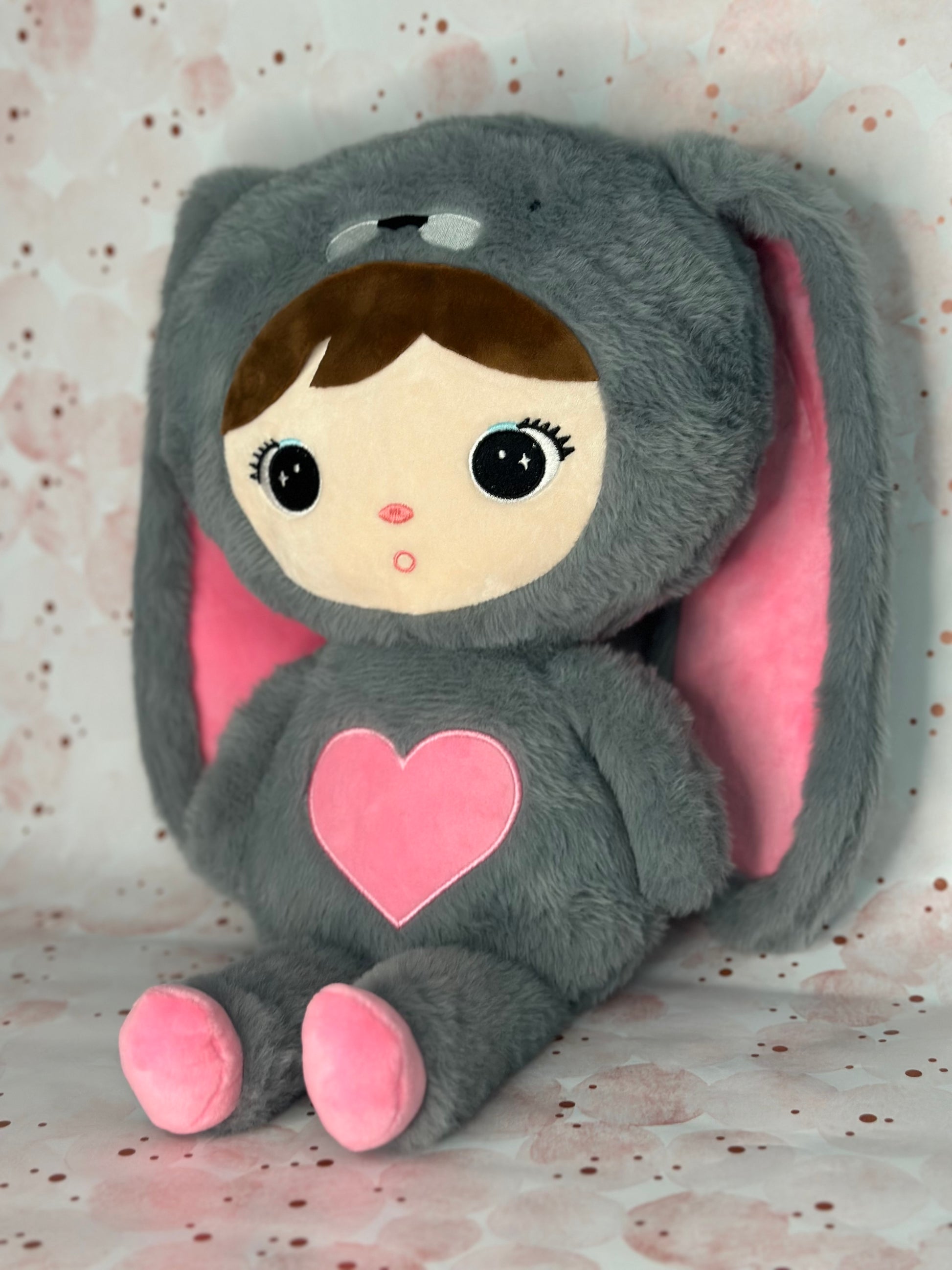 Plush toy with a gray outfit, pink heart, and pink ears on a patterned background