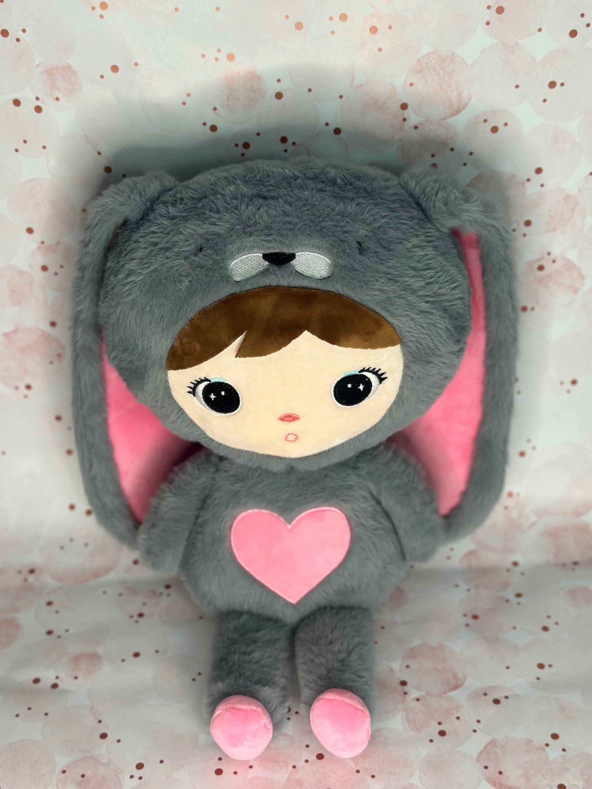 Plush toy in a gray costume with pink heart and ears on a light background