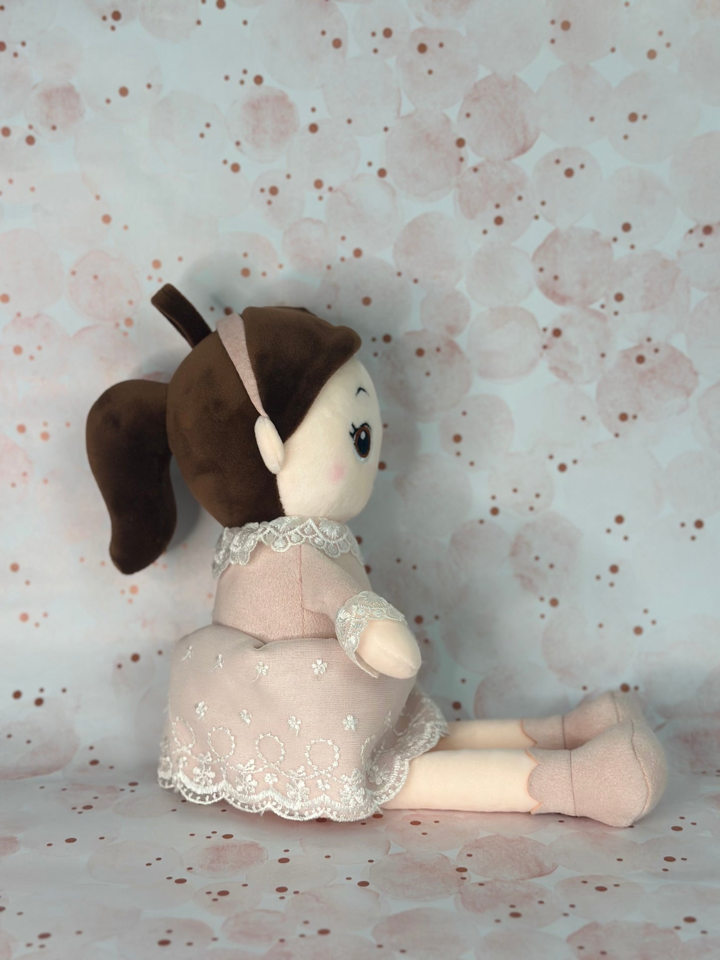 Stuffed toy doll in a dress sitting on a floral-patterned surface