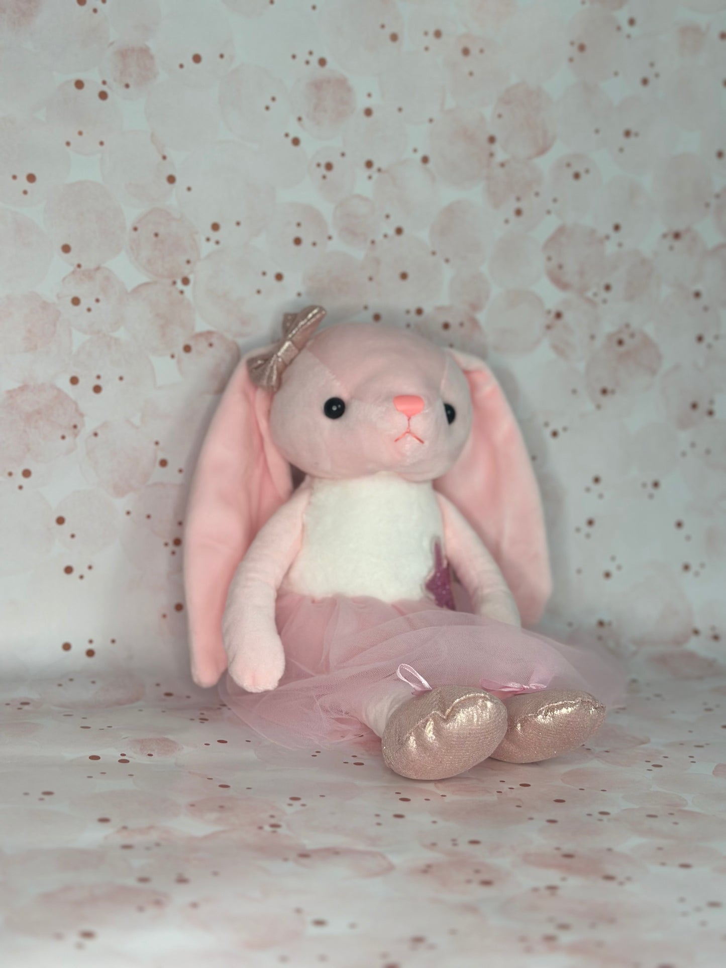 Pink bunny plush toy with a gold bow on a polka dot background