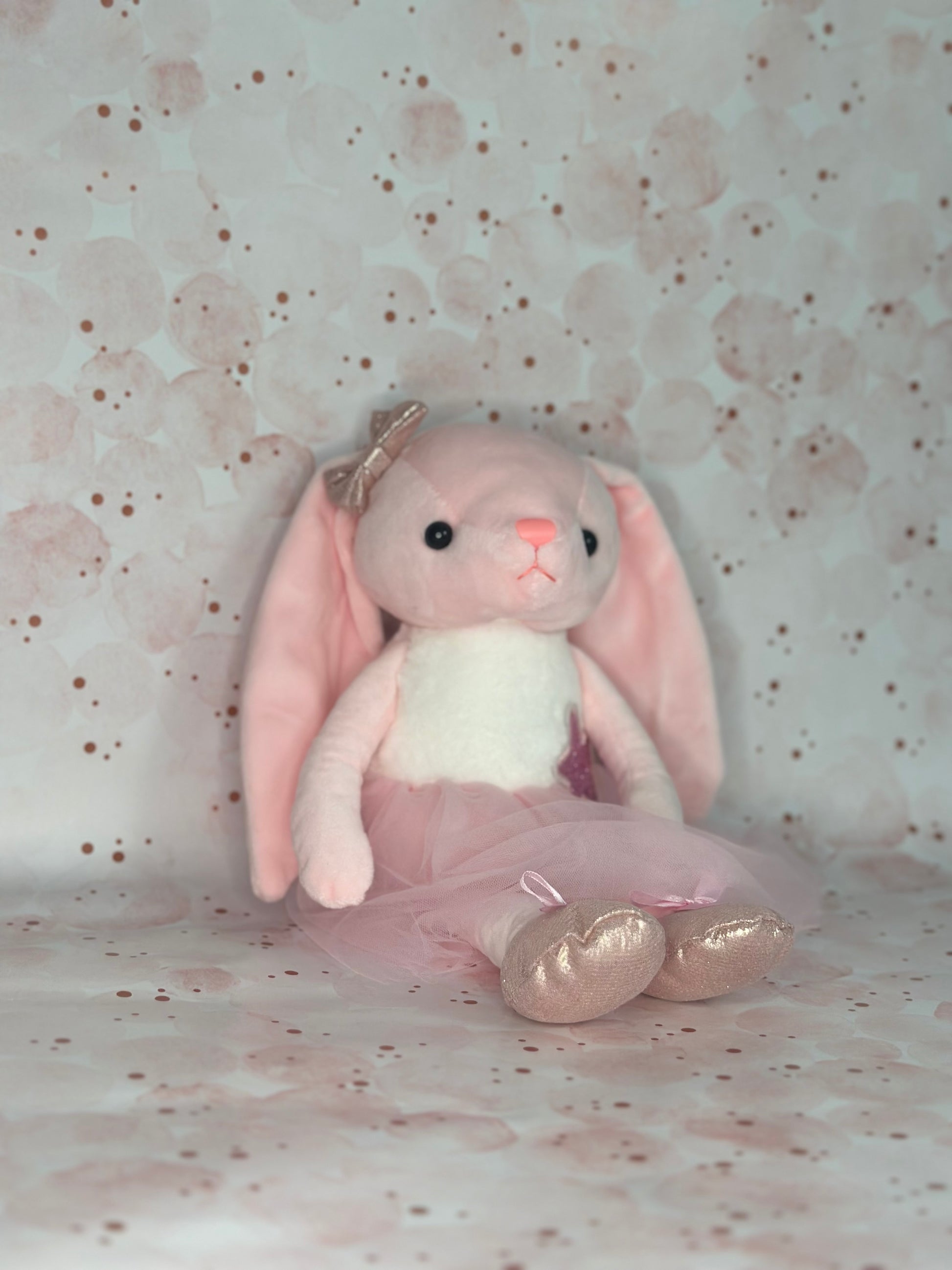 Pink bunny plush toy with a gold bow on a polka dot background