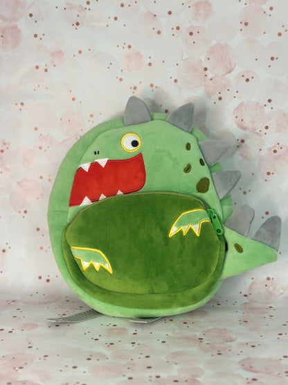 Green dinosaur-shaped backpack on a light pink background